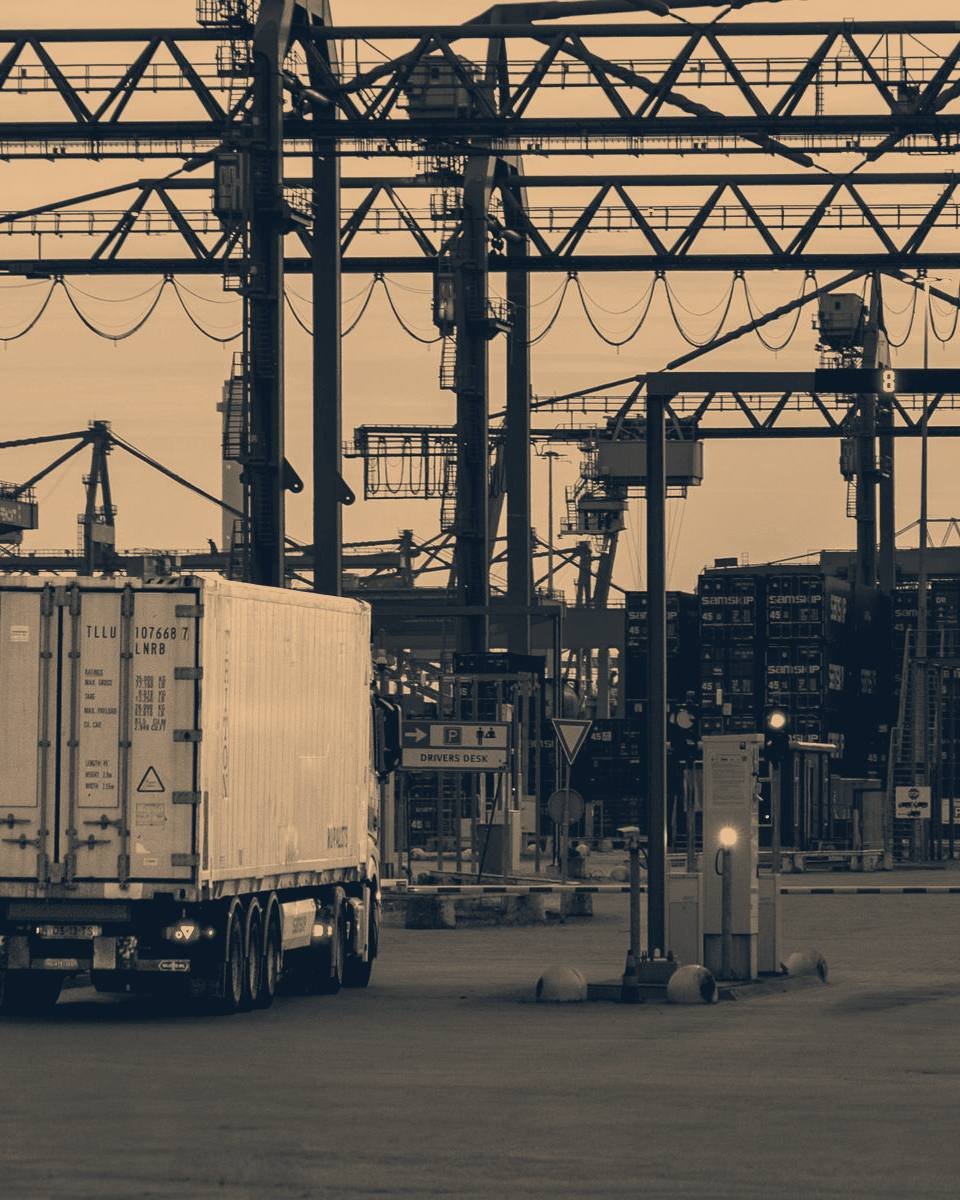 Ein Containertransport verlässt bei Dämmerung ein Hafenterminal.